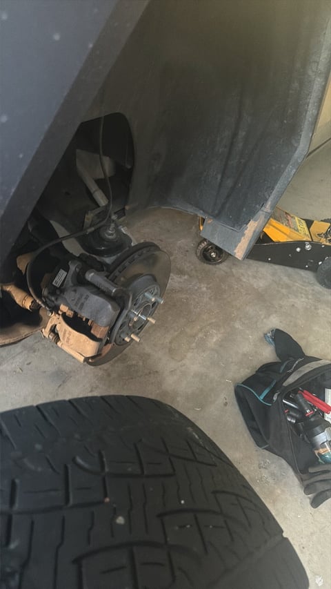 Close view of a Cybertruck wheel well with wheel removed, brake disc and caliper visible, tire and tools on the garage floor
