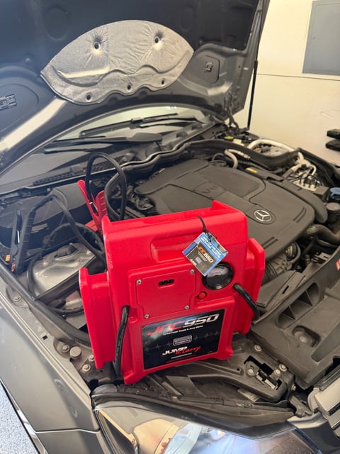 JNC950 Jump-N-Carry 12V jump pack clamped on a Mercedes-Benz V6 engine bay during a battery health and boost test in an Austin TX garage — All Hours Roadside mobile battery service