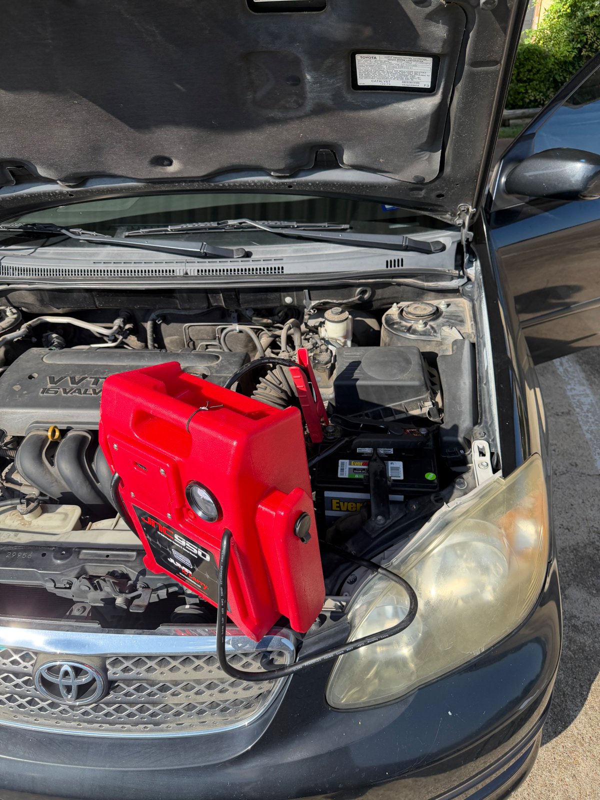 Clore JNC950 Jump-N-Carry commercial jump pack clamped to a Toyota Corolla EverStart Value 12V battery in a Dallas driveway — All Hours Roadside mobile jump start