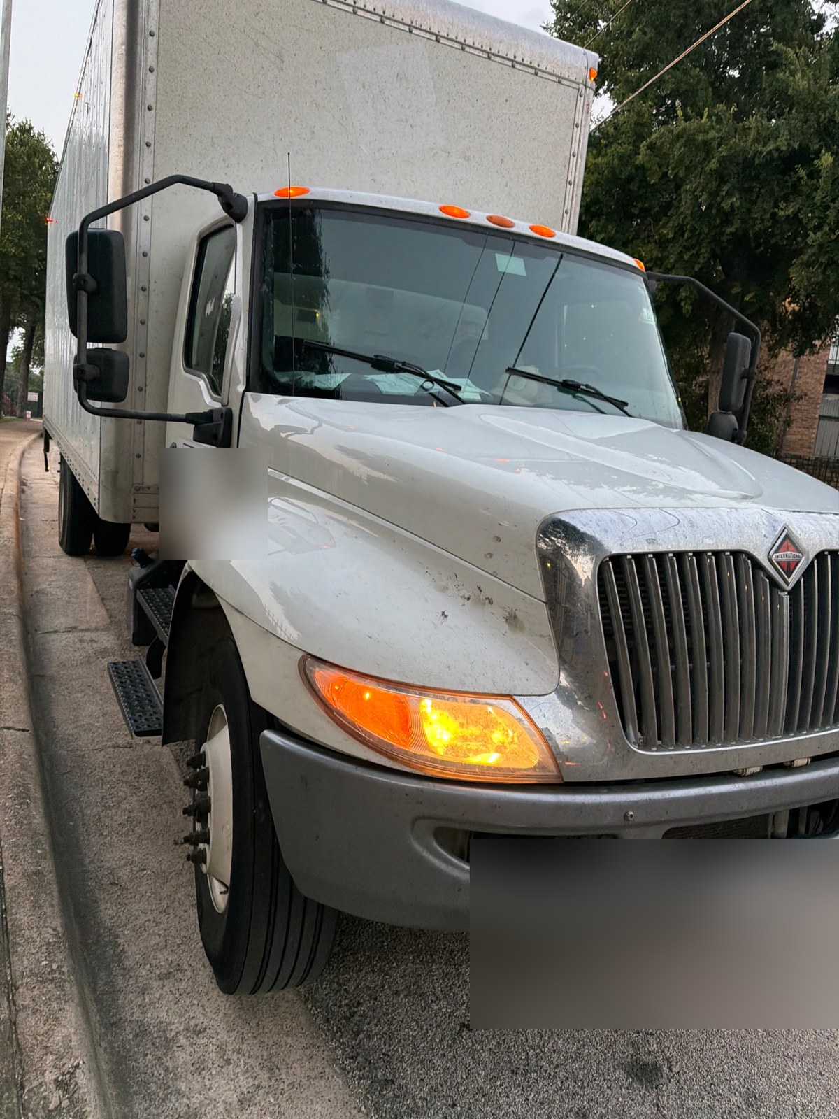 International MV series 26-foot box truck receiving a 12V medium-duty jump start from All Hours Roadside in DFW (license plate and DOT panel blurred for privacy)
