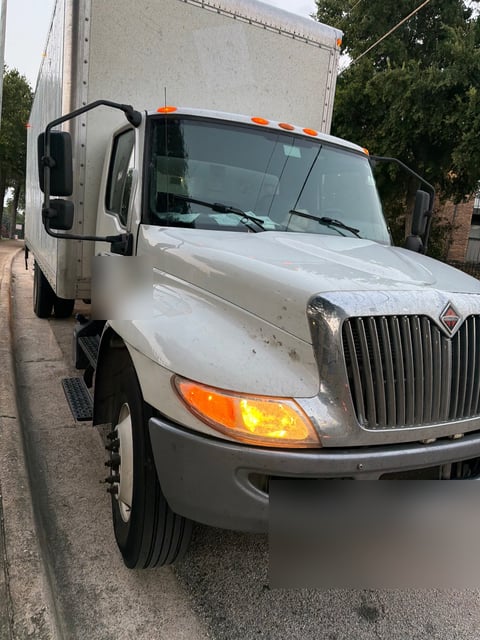 International MV series 26-foot box truck receiving a 12V medium-duty jump start from All Hours Roadside in DFW (license plate and DOT panel blurred for privacy)