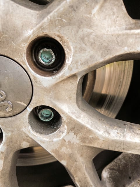 Two heavily corroded aluminum lug nuts seized deep inside a Jeep alloy wheel with brake rotor visible through the spokes — mobile stripped-lug extraction by All Hours Roadside in the Dallas–Fort Worth metro