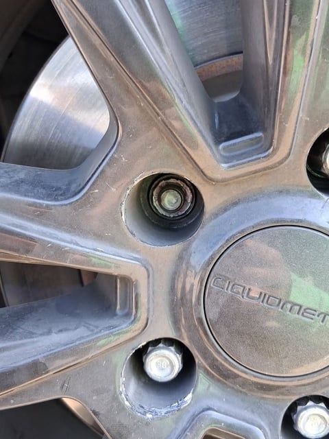 Close-up of a rounded and stripped lug nut swaged inside the lug pocket of a dark alloy wheel before extraction with a reverse-spiral socket during a mobile wheel-lock removal in Dallas Fort Worth by All Hours Roadside