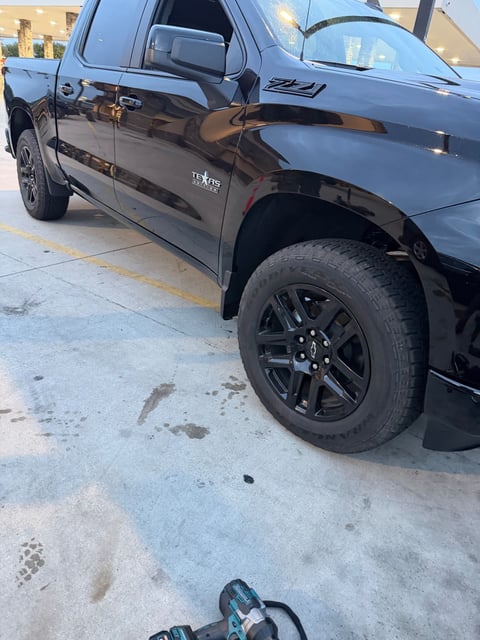 Black Chevrolet Silverado with a cordless impact wrench staged beside the front wheel during mobile tire service by All Hours Roadside