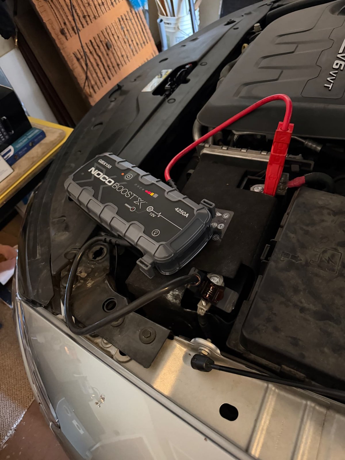 NOCO Boost X GBX155 jump pack with red and black clamps connected to an under-hood 12V car battery during a mobile jump start in Addison TX by All Hours Roadside