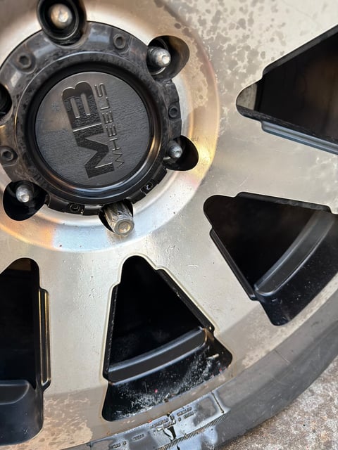 Close-up of a black KMC XD Series wheel on a GMC Sierra showing a spline-drive locking lug nut with the key missing — removed on-site by All Hours Roadside in DFW