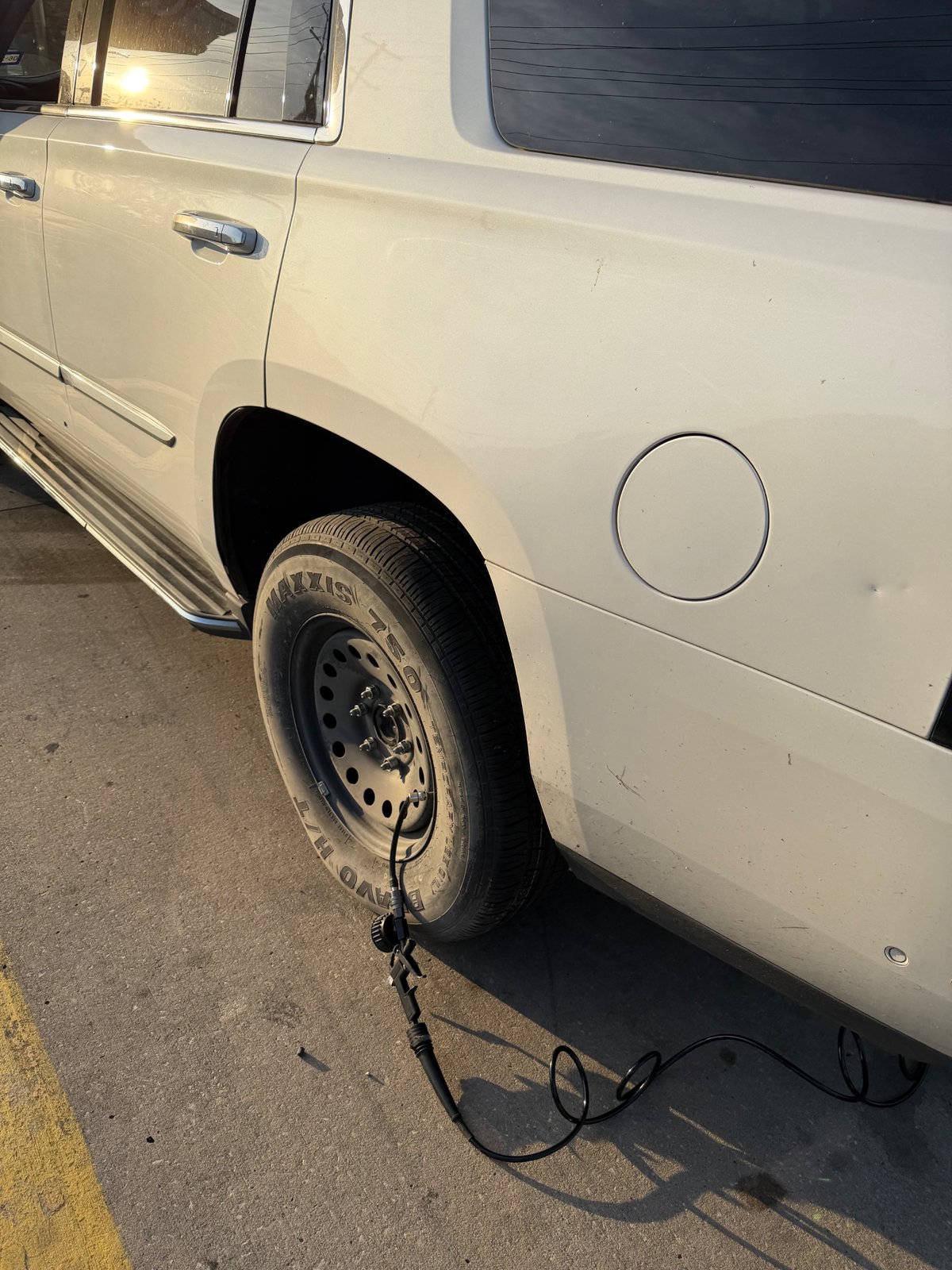 All Hours Roadside spare tire change on a white Cadillac Escalade in a Grapevine, TX parking lot — full-size spare mounted on the rear passenger side, portable 12V inflator topping off tire pressure roadside.