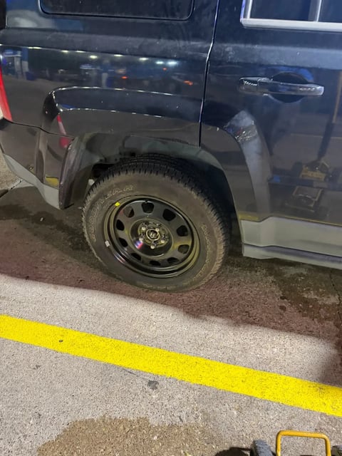 Goodyear spare tire mounted on the rear wheel of a dark SUV after a roadside tire change
