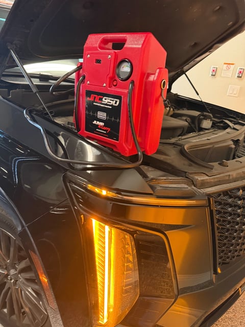 Red Clore JNC950 Jump-N-Carry jump pack set on the fender of a black SUV with the hood raised and the amber LED daytime running light lit during a mobile jump start in Southlake TX by All Hours Roadside