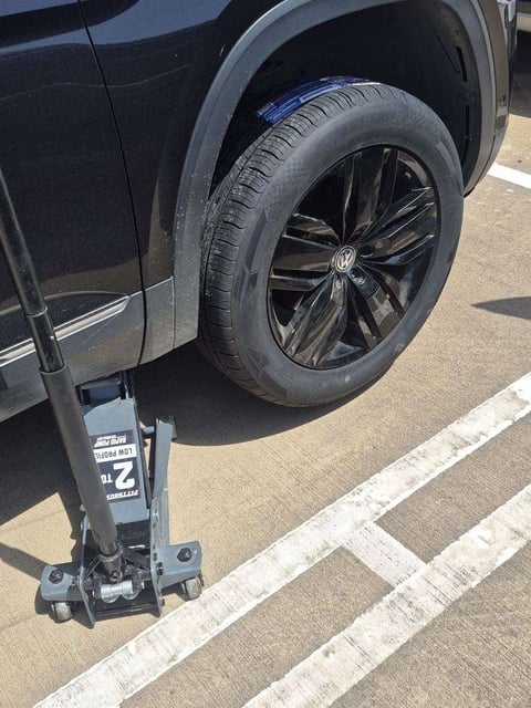 Black Volkswagen Atlas SUV lifted on a Pittsburgh 2-ton low-profile rapid pump floor jack with the full-size spare tire mounted after a roadside tire replacement by All Hours Roadside in Dallas, TX