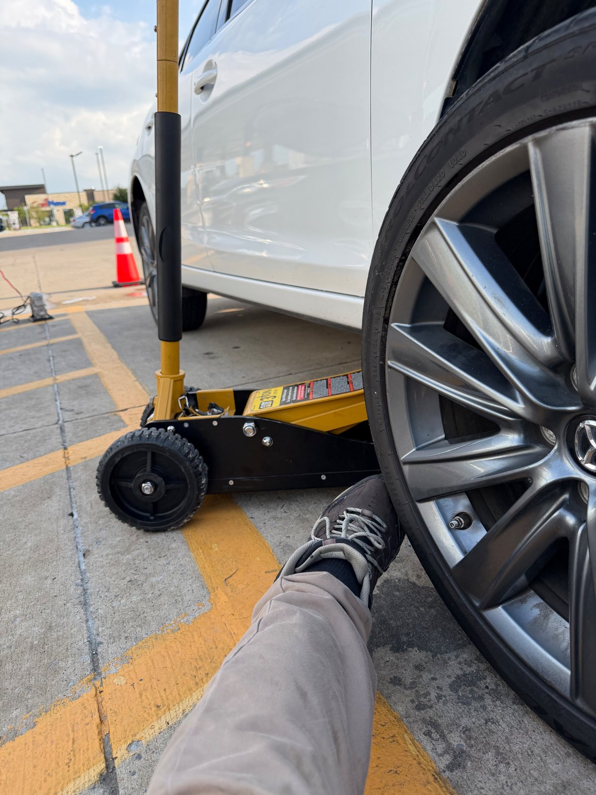Mercedes-Benz sedan raised on a floor jack in a DFW retail parking lot with a safety cone deployed by All Hours Roadside technician