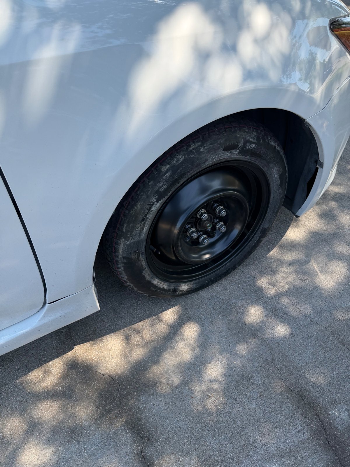 White sedan with a black steel donut spare tire mounted on the front passenger side after an on-site spare change by All Hours Roadside in Austin, TX