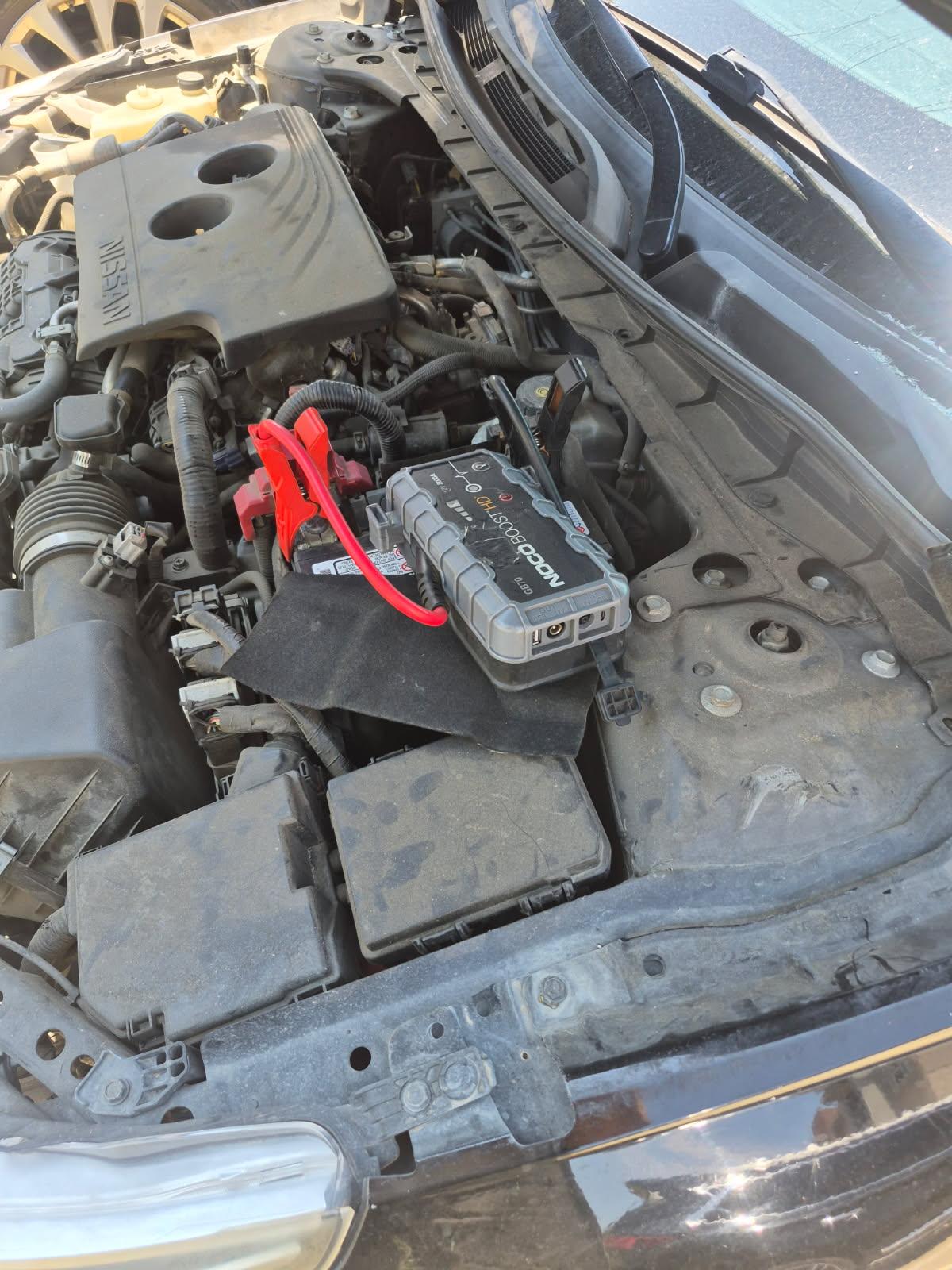 NOCO Boost HD GB70 lithium jump pack clamped to a Nissan sedan 12V battery in DFW with red engineering clamp on the positive post — All Hours Roadside mobile jump start