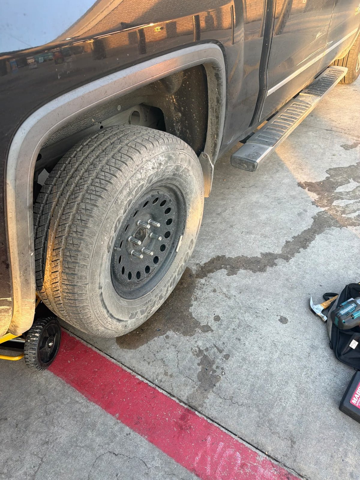 GMC Sierra 1500 lifted on a floor jack with the wheel off and spare tire being installed, KMC XD Series wheel, during a mobile tire change in the DFW metro by All Hours Roadside