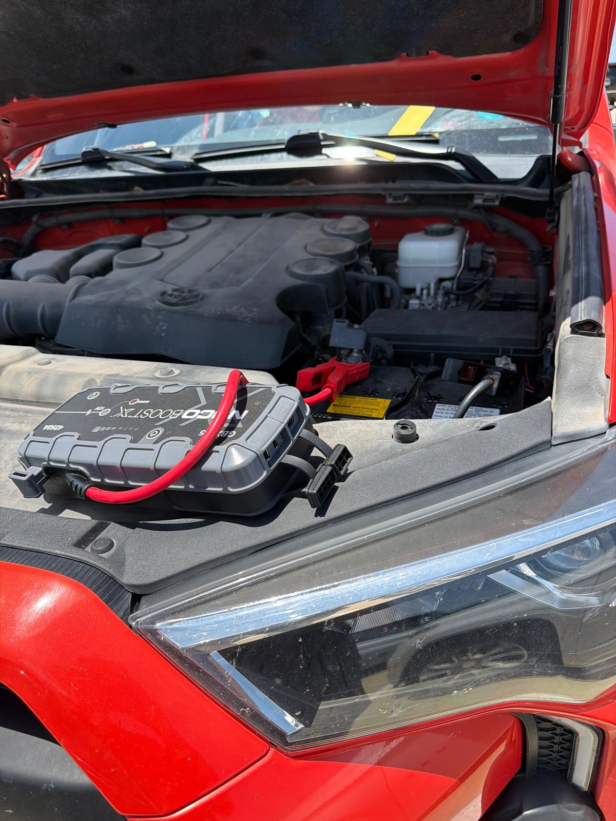 NOCO Boost X GBX55 1750A lithium jump pack clamped to a 12V battery under the hood of a red Toyota during a mobile jump start in Frisco TX — All Hours Roadside same-hour battery boost