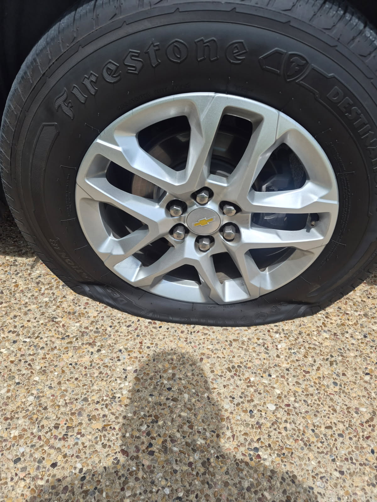 Chevrolet Equinox with a fully deflated Firestone Destination LE3 235/65R17 tire sitting flat on the rim in an Austin driveway, sidewall intact — mobile flat tire repair by All Hours Roadside