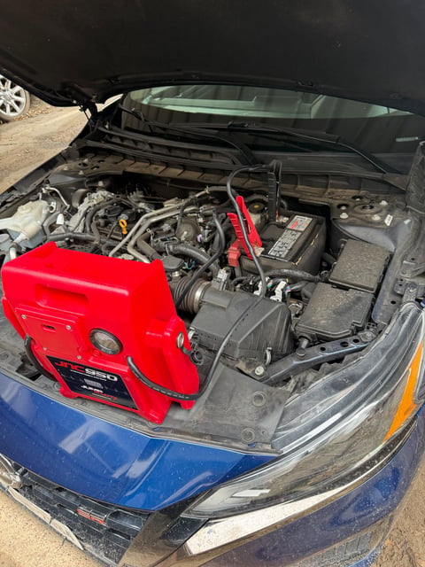 Clore JNC950 Jump-N-Carry commercial jump pack clamped to a blue Nissan Altima SR 12V battery in Plano TX — All Hours Roadside mobile jump start near Legacy West