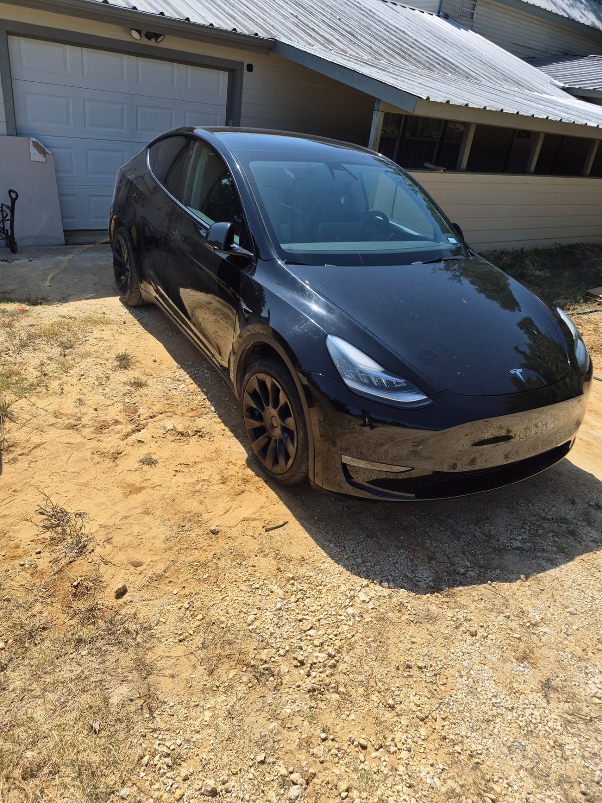Black Tesla Model Y fully lowered and sitting on a gravel driveway in front of a house after a completed mobile tire change in DFW