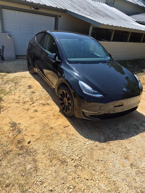 Black Tesla Model Y sitting level on all four wheels in a gravel driveway after a completed mobile tire change by All Hours Roadside in Dallas–Fort Worth, tools cleared and the vehicle ready to drive