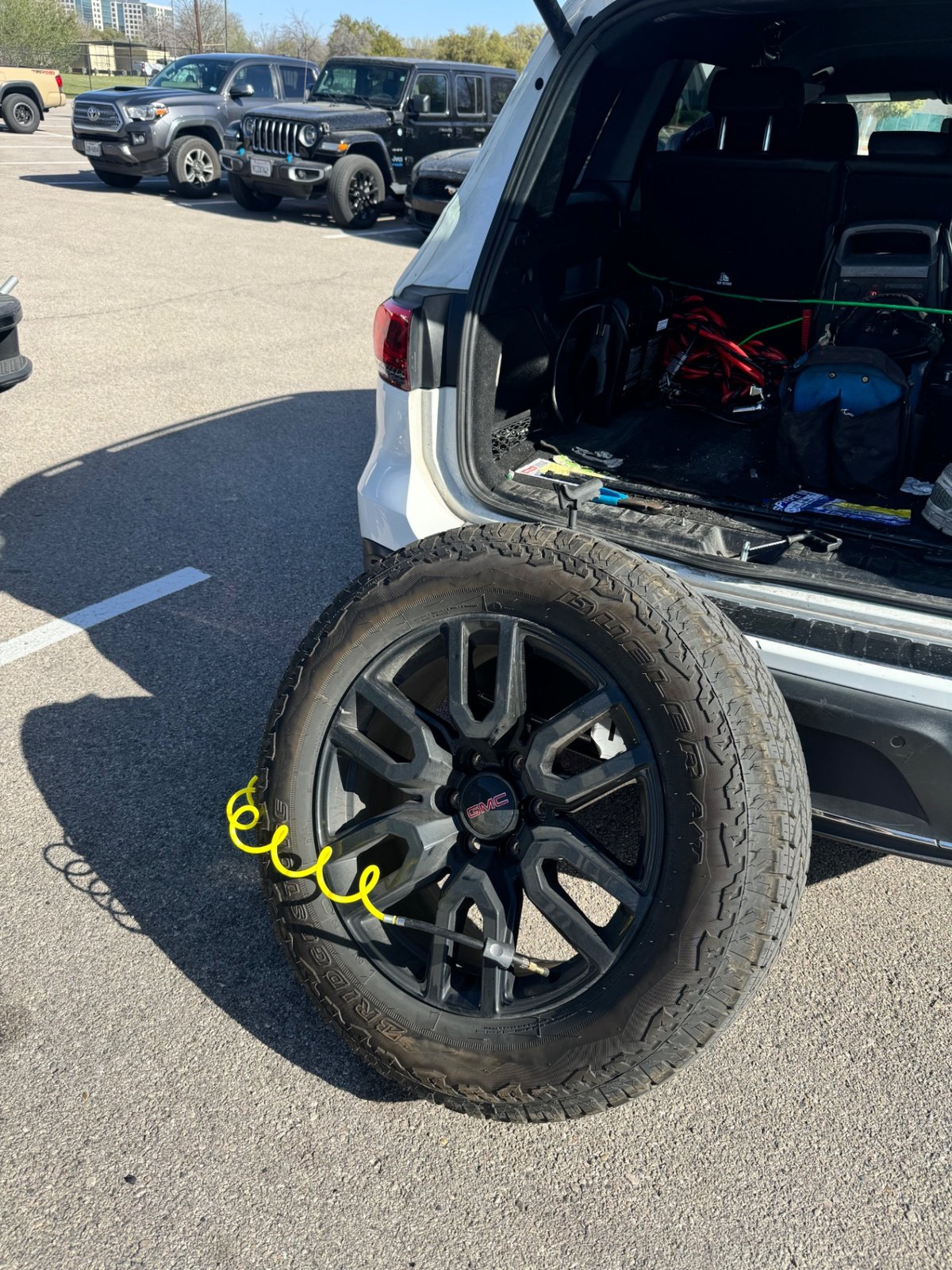 GMC SUV spare tire being inflated with a portable air compressor by an All Hours Roadside technician in a Dallas parking lot