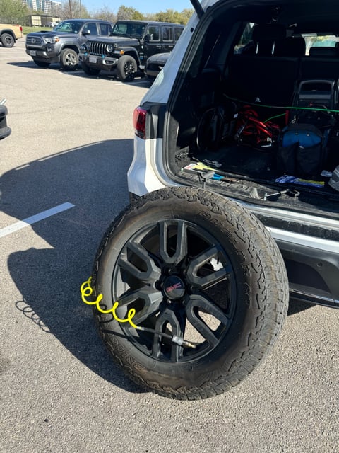 GMC pickup spare tire mounted and being aired up with a coil hose by an All Hours Roadside technician in a DFW parking lot