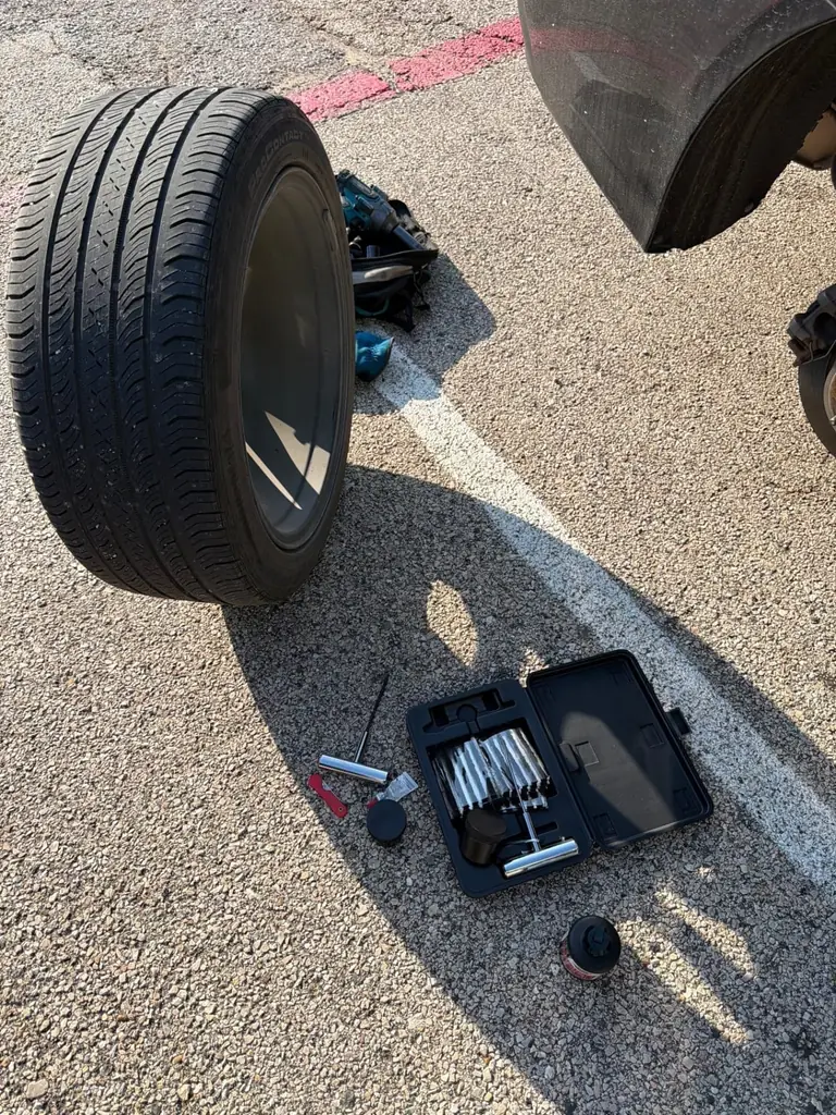 Tire standing on asphalt next to an open tire plug repair kit during a roadside puncture repair in DFW